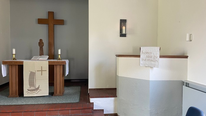 Ein Kirchenaltar mit Kreuz und Kerzen, daneben ein weißes Pult mit einem Schild.