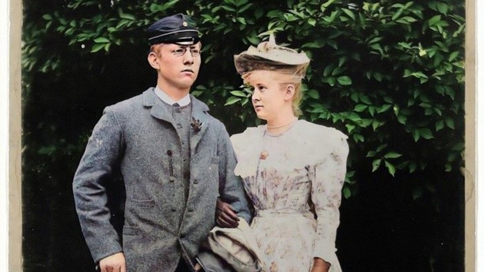 Et vintagepar står udendørs i tøj fra begyndelsen af 1900-tallet og poserer sammen i en frodig have.