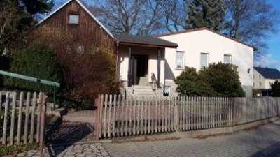 Ein malerisches weißes Haus mit einem Holzzaun, Stufen und einem Fahrrad, das dagegenlehnt an einem Kopfsteinpflasterweg steht.