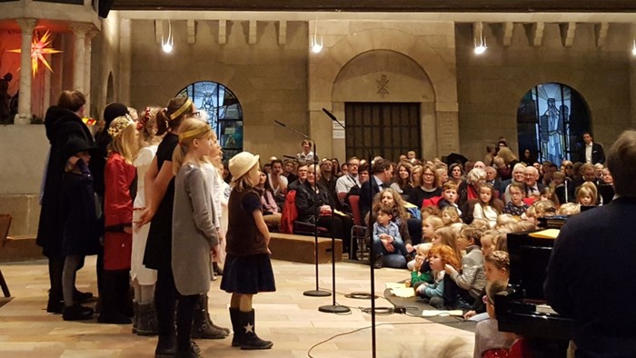 Eine Gruppe von Menschen singt in einem großen Raum, begleitet von einem Pianisten.