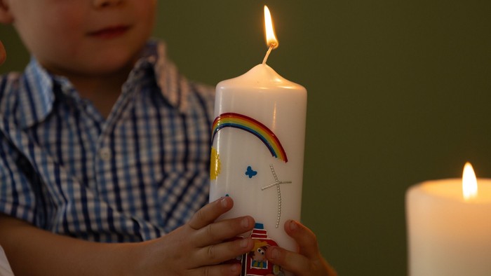 Ein Kind hält eine bunte Kerze mit angezündeter Flamme.