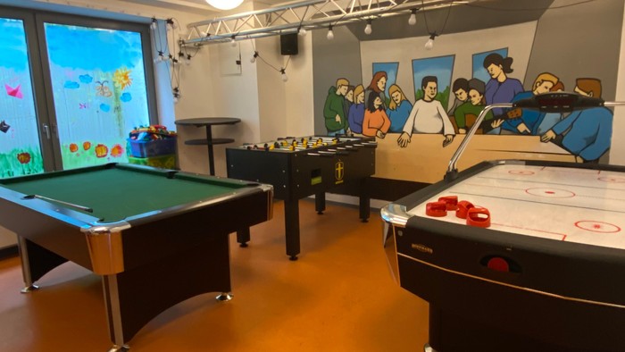 Ein Raum mit Billardtischen und Airhockey-Tischen, beleuchtet von Deckenlampen