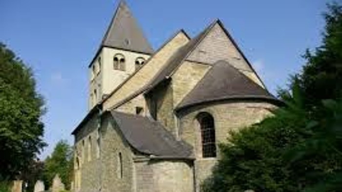 Das Bild zeigt eine alte Kirche mit spitzen Türmen und einem grasbewachsenen Friedhof.
