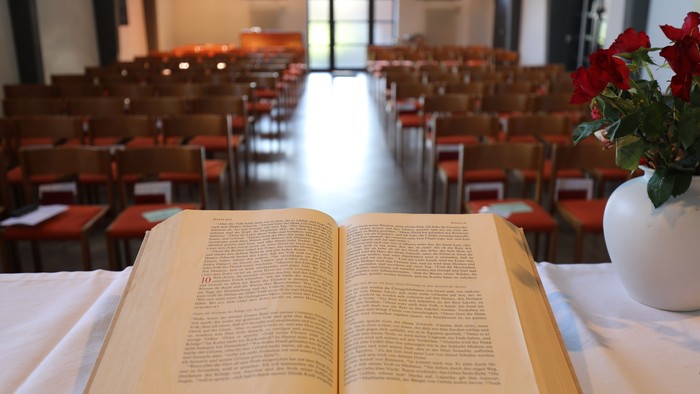 Offene Bibel auf Tisch in leerer Kirche mit Blumenstrauß