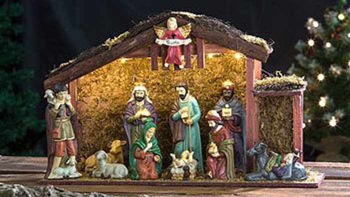 Eine Weihnachtskrippe mit Figuren, die in einem Stall mit Heu und einem Baum im Hintergrund dargestellt sind.