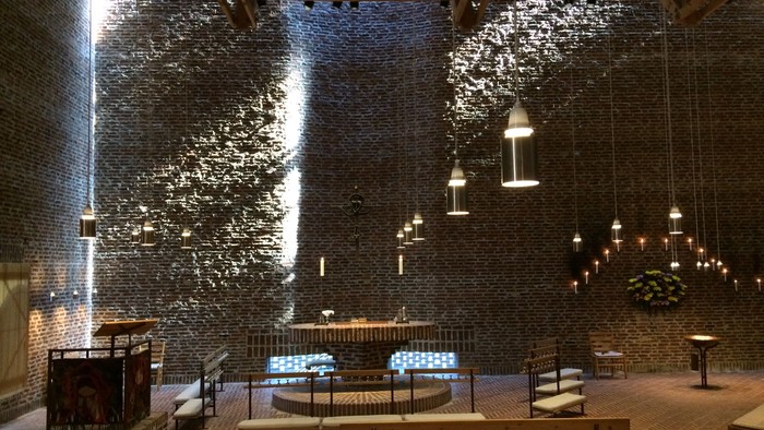 Indre del af en moderne kirke med høje vægge og hængende lys.