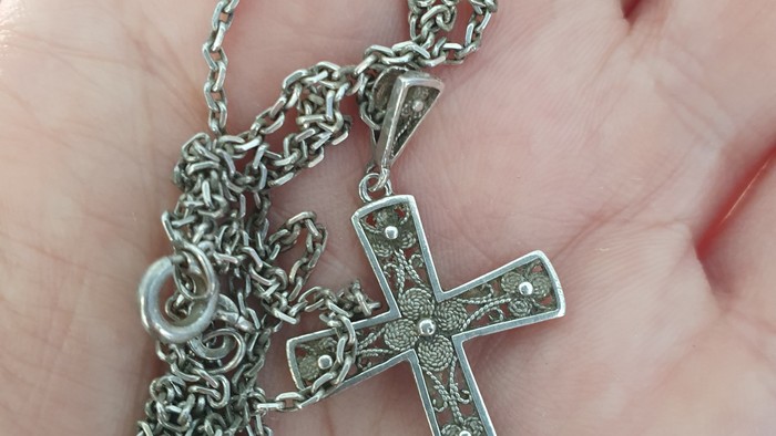 Kreuz aus Metall mit Kette in Handfläche 