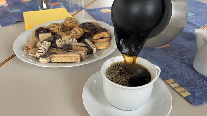 Hier sieht man einen Teller voll mit Keksen und wie eine Tasse Kaffee eingegossen wird.