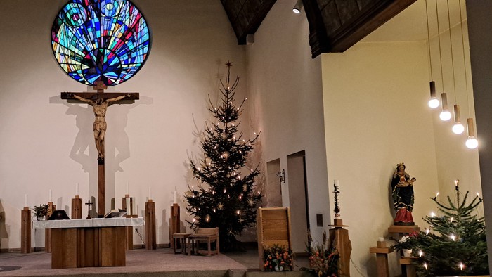 In der Kirche steht ein geschmückter Weihnachtsbaum unter einem großen Kirchenfenster.