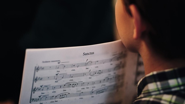 Eine Person liest konzentriert die Noten eines Chorstücks mit dem Titel *„Sanctus“*.