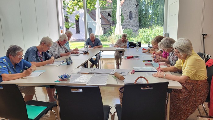 Seniorengruppe bastelt in hellem Raum mit Blick auf Garten