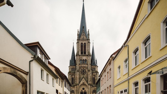 Eine hohe Kirche mit einem spitzen Turm steht zwischen zwei Gebäuden in einer engen Straße.