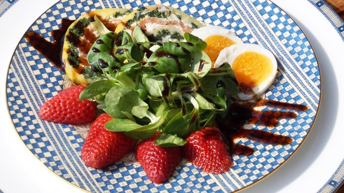 Teller mit Quiche, Salat, Erdbeeren und hartgekochtem Ei.