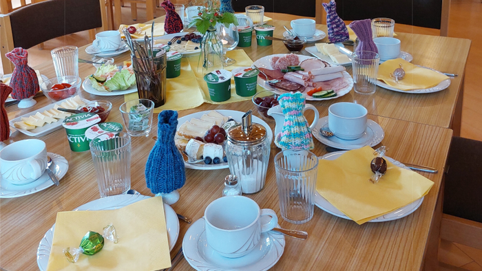 Liebevoll gedeckter Frühstückstisch in einem hellen, modernen Raum mit frischen Brötchen, Käse, Aufschnitt, Joghurt und Kaffee, dekoriert mit bunten Details