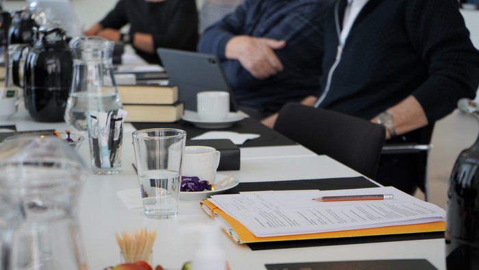 En gruppe af mennesker sidder ved et bord med notatblokke, penner og laptopter.