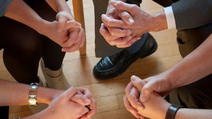 Ein Team formt einen Kreis und zeigt Zusammenhalt durch das Verschränken der Hände.