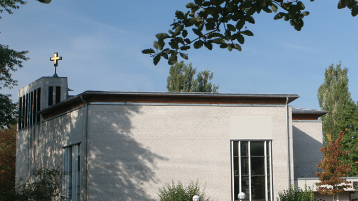 Kleine Kirche mit Kreuz auf dem Dach, umgeben von Bäumen und Gras