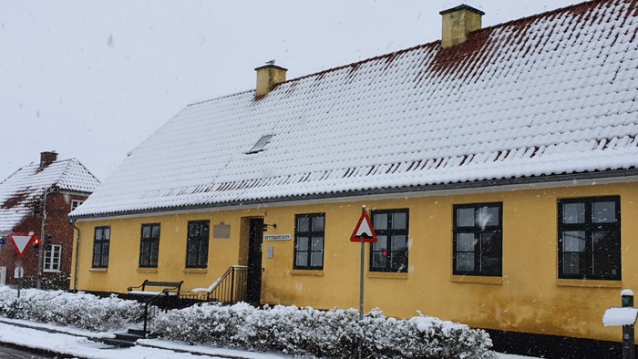 En guleg præget hus med snø på taket og omgivelser