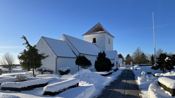 En snehvid kirke med klar blå himmel og en anlagt havegang.