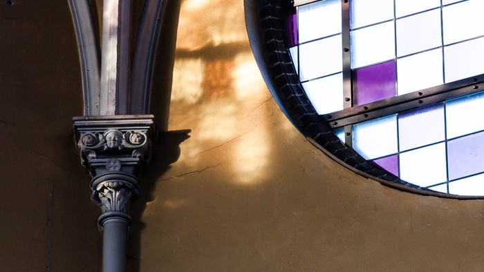 Ein verzierter Säulenschaft neben einem bunt gefärbten Kirchenfenster.