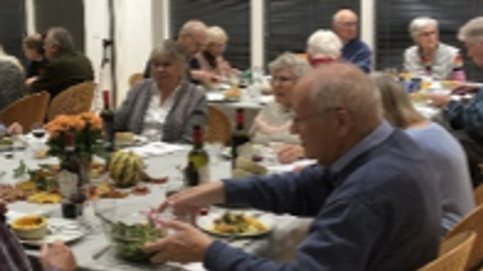 En gruppe ældre folk sidder sammen og spiser sammen i et lys og behageligt rum.