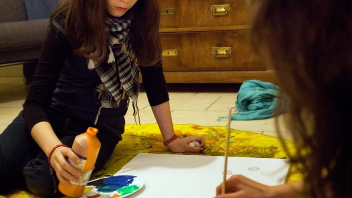 Zwei Personen erstellen gemeinsam Kunst mit Aquarellfarben und Pinseln auf großem Papier.