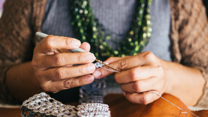 En person sitter og laver håndarbejde med strå.