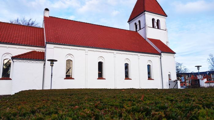 En hvid kirke med røde tag og tårn foran græsplæne