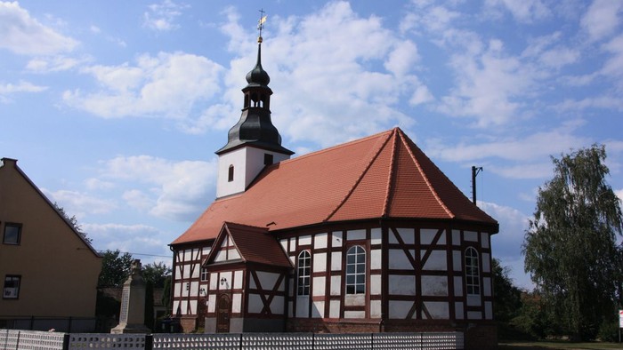 Weißes und rotes Holzhaus mit Kirche und blauen Himmel