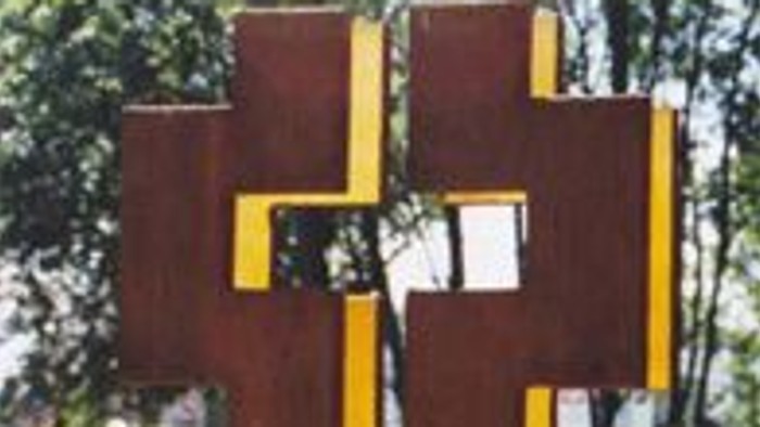 Ein großes Holzkreuz mit gelben Streifen in einem Garten.