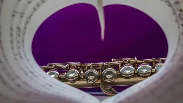 Nahaufnahme einer Flöte, eingerahmt von einem herzförmigen Notenblatt auf violettem Hintergrund.