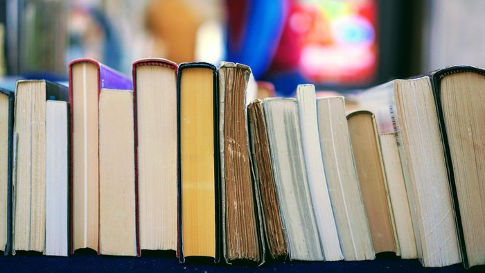 En række bøger, der står i en række på en hylde. I baggrunden ses noget, der ligner et kirkevindue med mosaik.