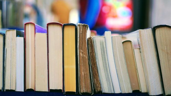 En række bøger, der står i en række på en hylde. I baggrunden ses noget, der ligner et kirkevindue med mosaik.