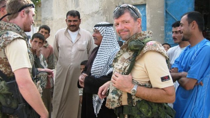 En gruppe mænd i militærudstyr og traditionelt tøj samlet udendørs, som ser ud til at interagere i et muligvis konfliktramt område.