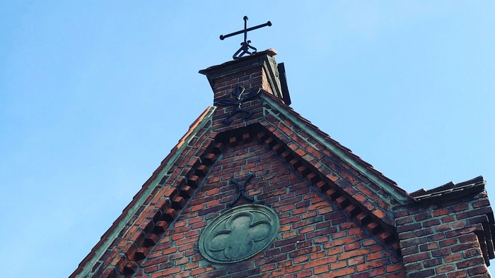 Ein Ziegelgebäude mit Wetterhahn und dekorativem Wappen auf dem Giebel.
