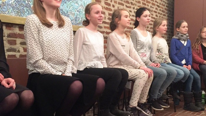 En gruppe unge piger sidder i en hal og smiler til kameraet