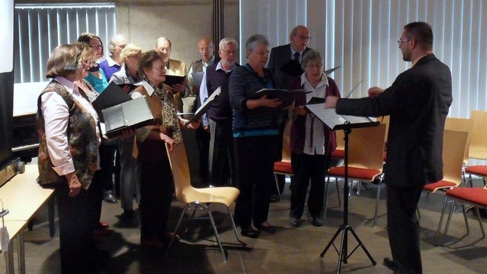 Ein Mann leitet einen Chor, der Noten liest