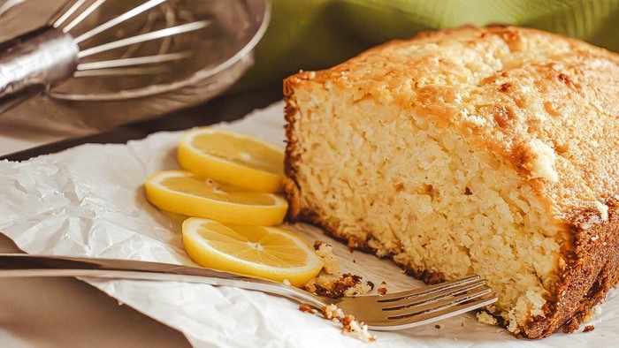A slice of lemon cake with lemon slices and a fork on a napkin.
