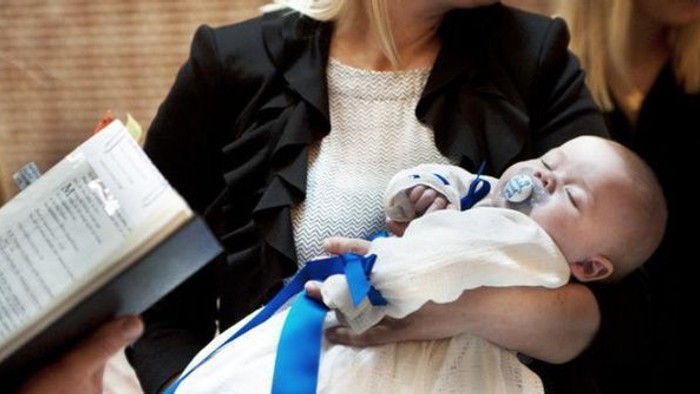 En kvinde holder et spæd barn og en bog, mens hun er omgivet af andre kvinder.