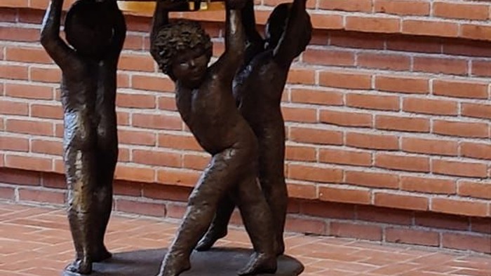 Bronzefigur af to børn, der bærer en plate på et murstenvægge