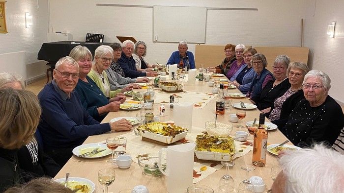 En gruppe ældre folk spiser sammen i en stor hall.