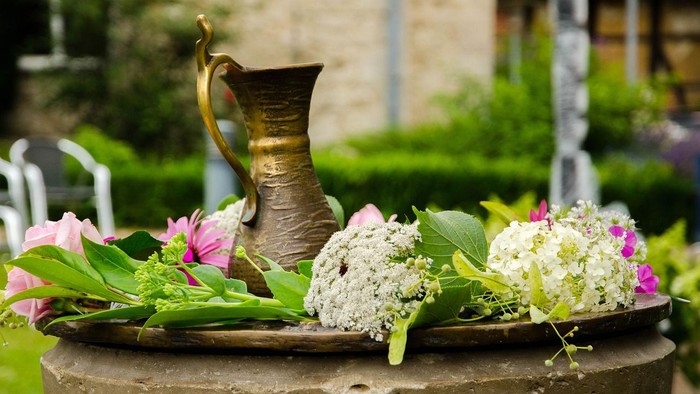 Blumenarrangement mit Vasen auf steinernem Sockel im Garten