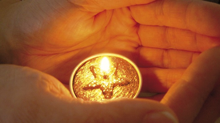 Eine Hand hält eine leuchtende Münze mit einem Kreuzsymbol