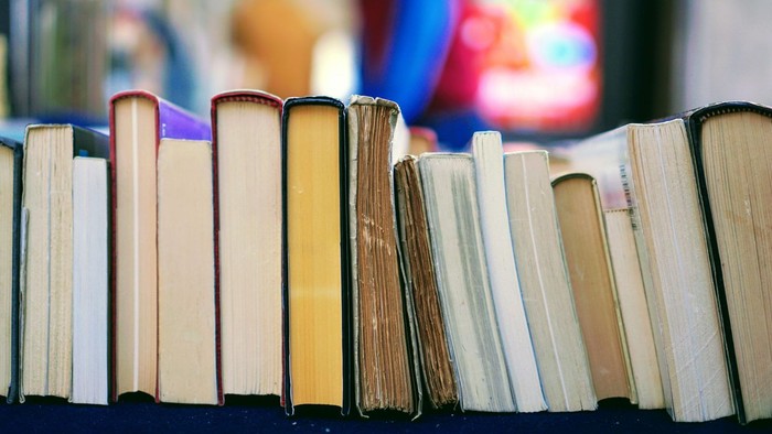 En række bøger, der står i en række på en hylde. I baggrunden ses noget, der ligner et kirkevindue med mosaik.