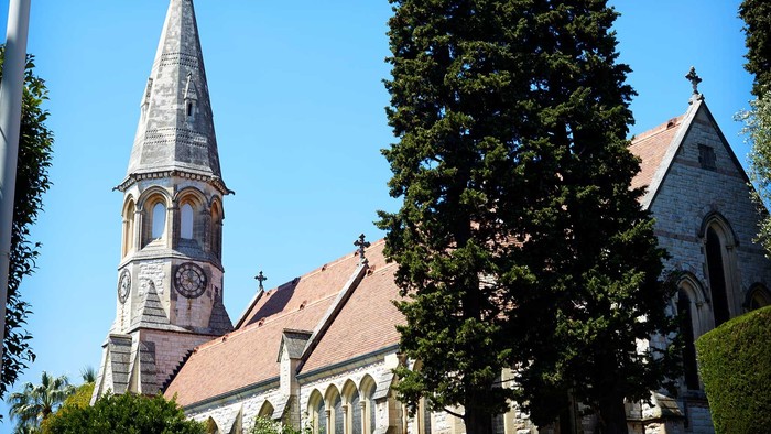 En kirke med spir med tårn og klokke, omgivet af træer og buske