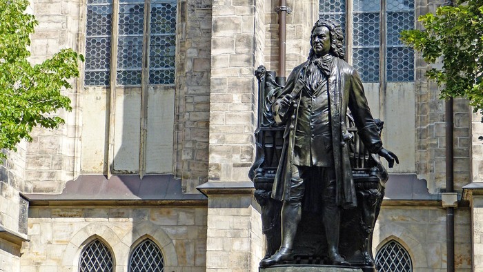 En statue af en historisk person i kjortel står fremtrædende foran en stor stenkirke med høje vinduer.