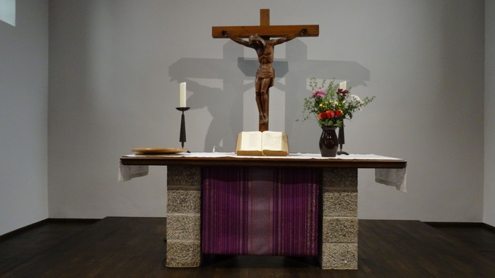Ein Altar mit Kruzifix, Kerze und Blumen in einem schlichten Raum
