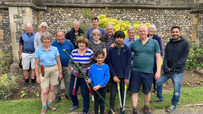 Group of people posing with gardening tools in front of stone building