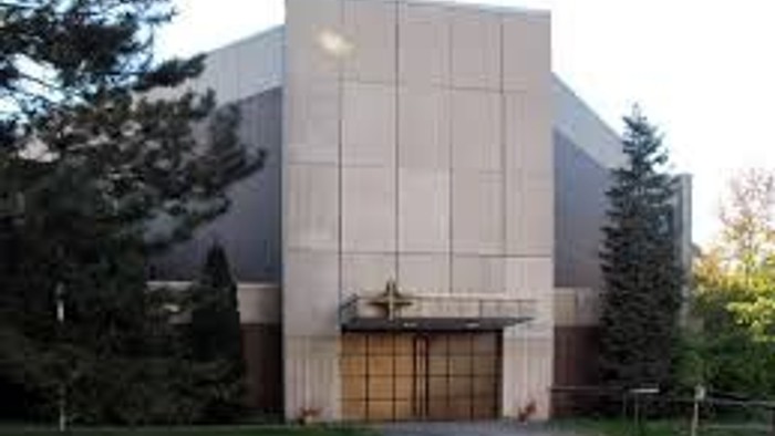 Das Bild zeigt ein modernes Gebäude mit großen Fenstern und einem Baum davor.