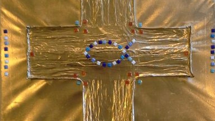 Goldenes Kreuz mit blauen Perlen auf weißem Tuch